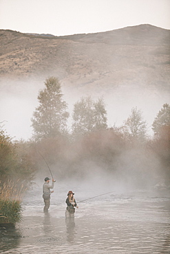 A couple, a man and woman standing in mid stream flyfishing in a river.