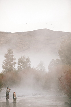 A couple, a man and woman standing in mid stream flyfishing in a river.