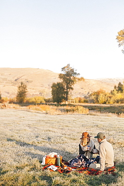 A couple, a man and woman having a winter picnic, sitting on a tartan rug.