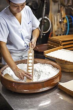 A small artisan producer of wagashi. A man mixing a large bowl of ingredients and pressing the mixed dough into moulds in a commercial kitchen, Japan