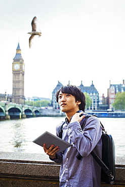 Young Japanese man enjoying a day out in London, standing on the Queen's Walk by the River Thames, United Kingdom