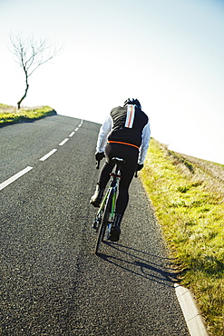 A cyclist pedalling along a country road, rear view. 