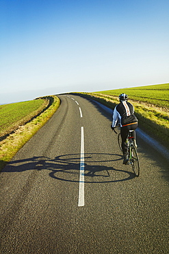 A cyclist pedalling along a country road, rear view. 