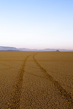 Tyre tracks in a desert landscape with mountains in the distance.