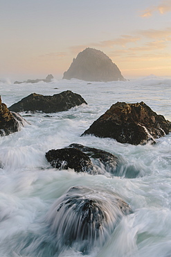 Seascape with breaking waves over rocks at dusk.