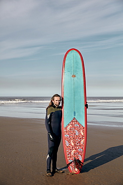 Portrait of a man holding a decorated surf board on a sandy beach, United Kingdom