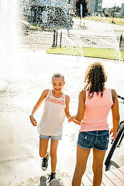 Smiling girls playing in public fountain in summer, United States of America