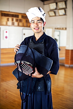 Male Japanese Kendo fighter standing in a gym, holding Kendo mask, looking at camera, Kyushu, Japan