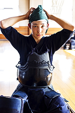 Male Japanese Kendo fighter kneeling on floor, wearing breastplate and tying headscarf, looking at camera, Kyushu, Japan