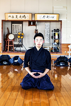 Male Japanese Kendo fighter kneeling on wooden floor, meditating, Kyushu, Japan