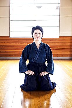 Female Japanese Kendo fighter kneeling on wooden floor, looking at camera, Kyushu, Japan