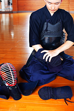 Male Japanese Kendo fighter kneeling on wooden floor, putting on Kote, hand protectors, Kyushu, Japan