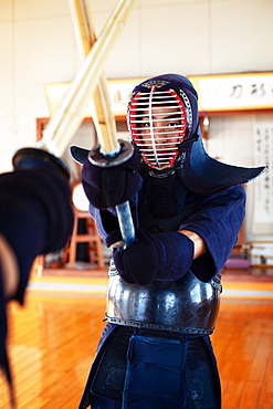 Two Japanese Kendo fighters wearing Kendo masks practicing with wood sword in gym, Kyushu, Japan