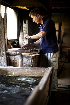 Japanese man in a workshop, holding a wooden frame with pressed pulp, making traditional Washi paper, Kyushu, Japan