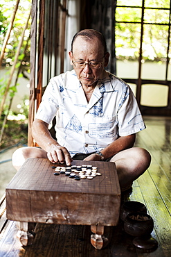 Japanese man sitting on floor on porch of traditional Japanese house, playing Go, Kyushu, Japan