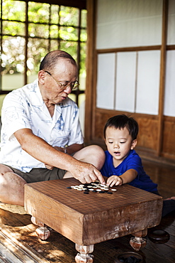 Japanese man and little boy sitting on floor on porch of traditional Japanese house, playing Go, Kyushu, Japan