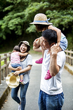 Japanese girl, smiling woman holding hat and man carrying toddler on his shoulders standing on wooden bridge, Kyushu, Japan