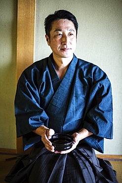 Japanese man wearing kimono kneeling on floor, holding tea bowl during tea ceremony, Kyushu, Japan