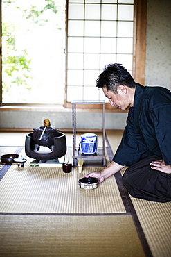 Japanese man wearing traditional kimono kneeling on floor, holding tea bowl, during tea ceremony, Kyushu, Japan