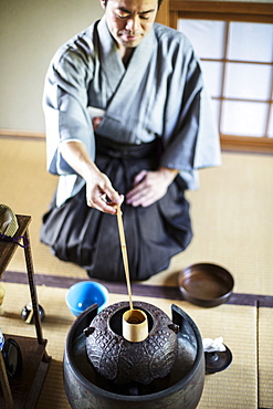 Traditional Japanese Tea Ceremony, man wearing kimono sitting on floor, using a Hishaku, a bamboo ladle, to pour hot water, Kyushu, Japan