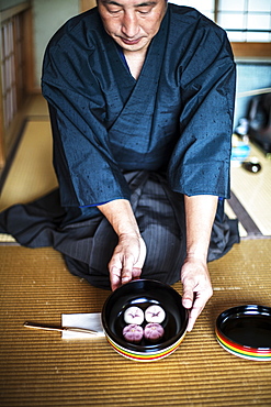 Japanese man wearing traditional kimono knelling on floor, holding a bowl with Wagashi, sweets traditionally served during a Japanese Tea Ceremony, Kyushu, Japan