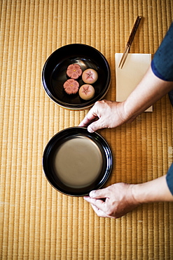 High angle close up of man knelling on floor, holding a bowl with Wagashi, sweets traditionally served during a Japanese Tea Ceremony, Kyushu, Japan