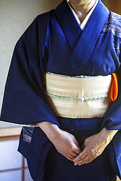 Close up of Japanese woman wearing traditional bright blue kimono with cream coloured obi kneeling on floor, Kyushu, Japan