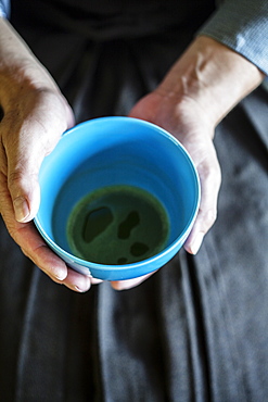 High angle close up of Japanese man wearing traditional kimono kneeling on floor holding blue tea bowl during tea ceremony, Kyushu, Japan