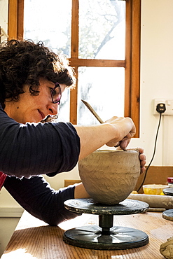 Woman sitting in her ceramics workshop, working on clay vase, England