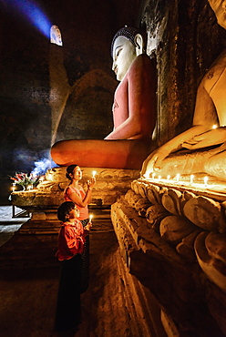 Asian mother and daughter lighting candles in temple