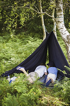 Two boys camping in the New Forest lying under a canvas shelter, Hampshire, England