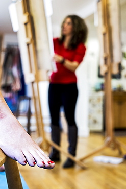 Close up of a bare female foot with red varnished toenails, a model at a life drawing class at art school. An artist working in the background, Oxfordshire, England