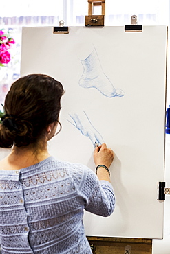 Rear view of woman standing at easel, drawing human hand and foot, Oxfordshire, England