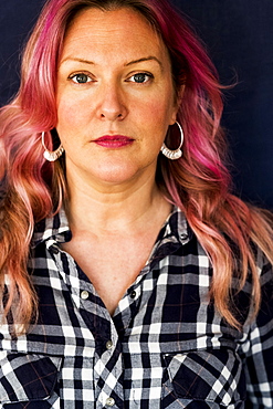 Portrait of woman with long blond wavy hair with pink streaks wearing black and white checked shirt and hoop earrings, Oxfordshire, England