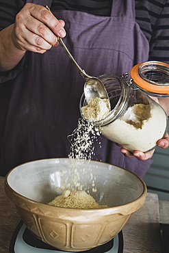 High angle close up of person pouring sugar into mixing bowl with baking ingredients, England