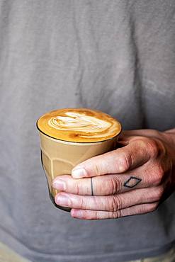 Close up of person with tattooed finger holding glass of cafe latte