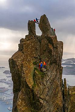 A group of people climbing on the Svolvaer Goat, 150-metre (490 ft), a jagged pinnacle high above the landscape of the Lofoten, Austvagoy, Lofoten Islands, Norway