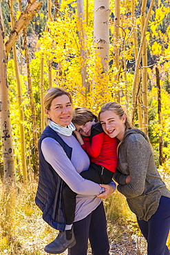 A mature woman, boy and girl, a mother and her two children in woodland, aspen trees in autumn colour,