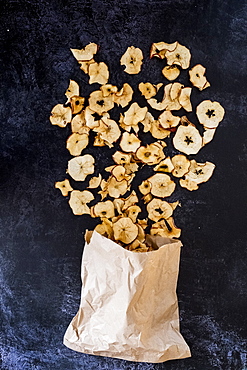 High angle close up of paper bag and dried slices of apple on dark background