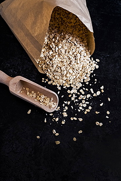 High angle close up of paper bag with oats and wooden spoon on dark background