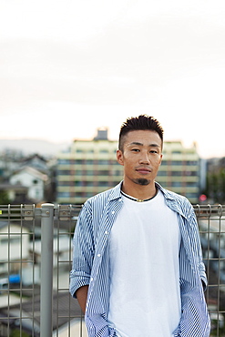 Young Japanese man standing on a rooftop in an urban setting, looking at camera, Fukuoka, Kyushu, Japan