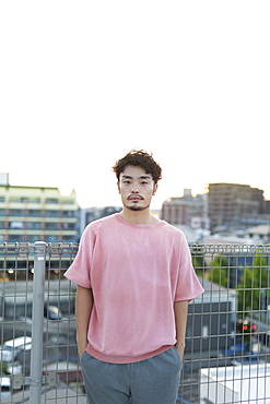 Young Japanese man standing on a rooftop in an urban setting, looking at camera, Fukuoka, Kyushu, Japan