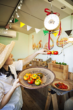 Japanese woman wearing hat working in a farm shop, weighing fresh vegetables, Kyushu, Japan