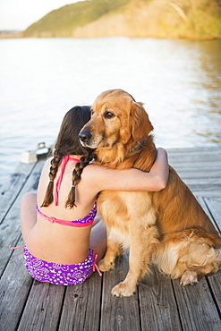 A young girl and a golden retriever dog sitting on a jetty, Austin, Texas, USA