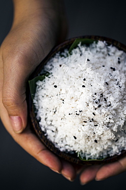 High angle close up of hand holding coconut flesh and black sesame seeds used as a body scrub, Thailand