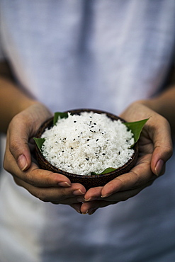 High angle close up of hand holding coconut flesh and black sesame seeds used as a body scrub, Thailand