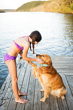 A girl in a bikini with a golden retriever dog lifting its paw up, Austin, Texas, USA