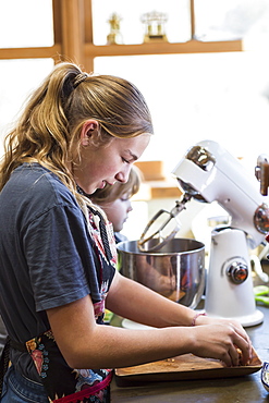 A teenage girl and her 6 year old brother in a kitchen, using a mixing bowl, United States