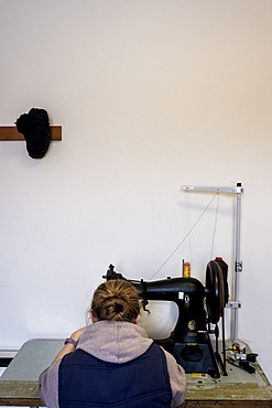 Rear view of female saddler sitting in workshop, sewing on saddlery sewing machine, Berkshire, United Kingdom