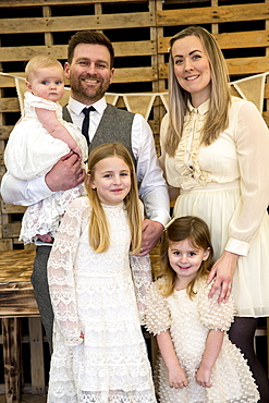 Portrait of smiling parents with their three young daughters during naming ceremony in an historic barn